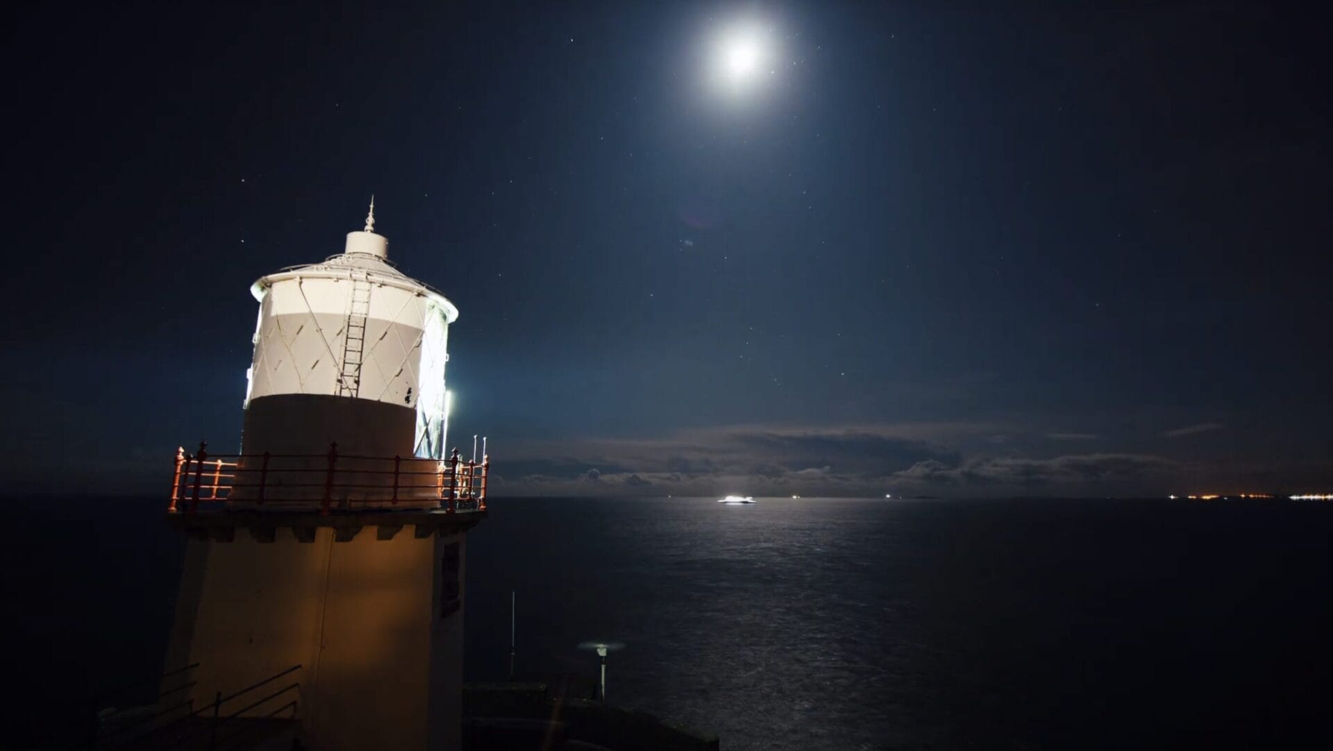 A lighthouse at night with moonlight reflected on the water